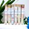Whole Self Aromatherapy's bath salts in test tubes on a white towel, with greenery in the background and a blue flower to the right.